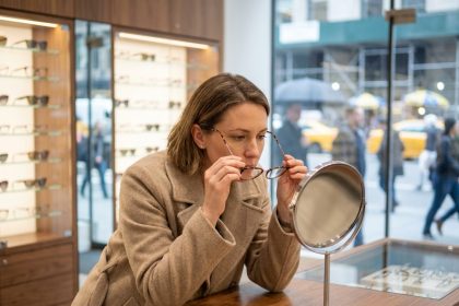Femme essayant des montures de lunettes dans une opticien en centre-ville avec vitrines de créateurs